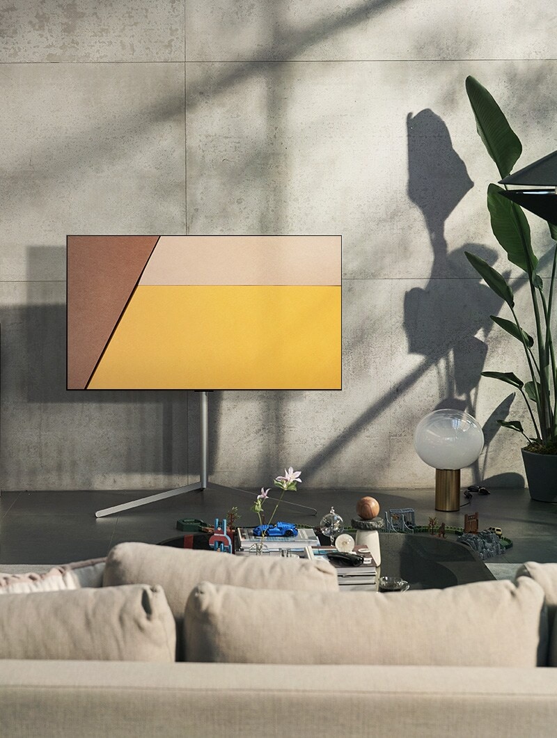 Een LG OLED televisie staat in een moderne grijze woonruimte tegen een raam met zicht op een zwembad. Een LG OLED televisie staat in een neutrale leefruimte met zichtbare bakstenen, houten details en groen.