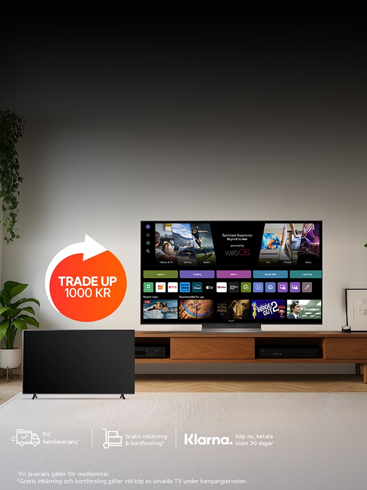 Ett modernt vardagsrum med en LG smart-TV som står på en TV-bänk i trä och visar olika streamingappar på skärmen. En subwoofer står på golvet till vänster. En röd cirkel med texten "BYT UPP TILL LG OLED TV" syns på bilden. Bakgrunden är minimalistisk med neutrala färger och en krukväxt delvis synlig till vänster.