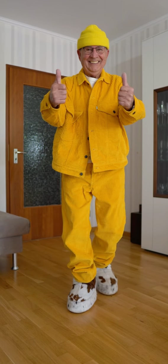 Ein Mann in einem leuchtend gelben Outfit, der den Daumen nach oben streckt und damit Zuversicht und Freude ausdrückt.