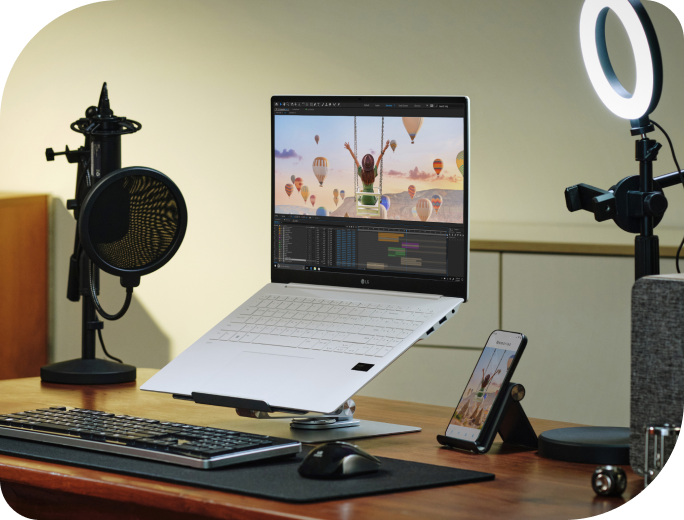 LG gram nằm trên bàn có micro và đèn chuông, có màn hình chỉnh sửa video, cho hiệu suất cao dù trọng lượng nhẹ.