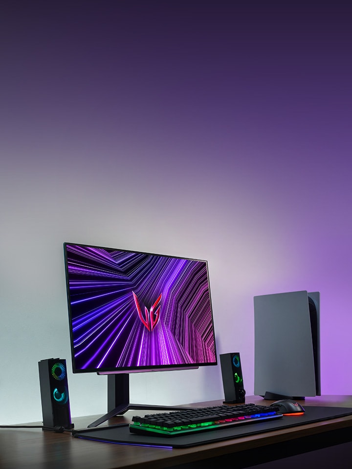27GS95QE-B on a desk with a PS5, lit up by a purple glow in the background
