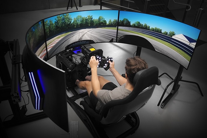 Curved UltraGear OLED monitor screens dispaying a racing simulater, with player sat in the middle