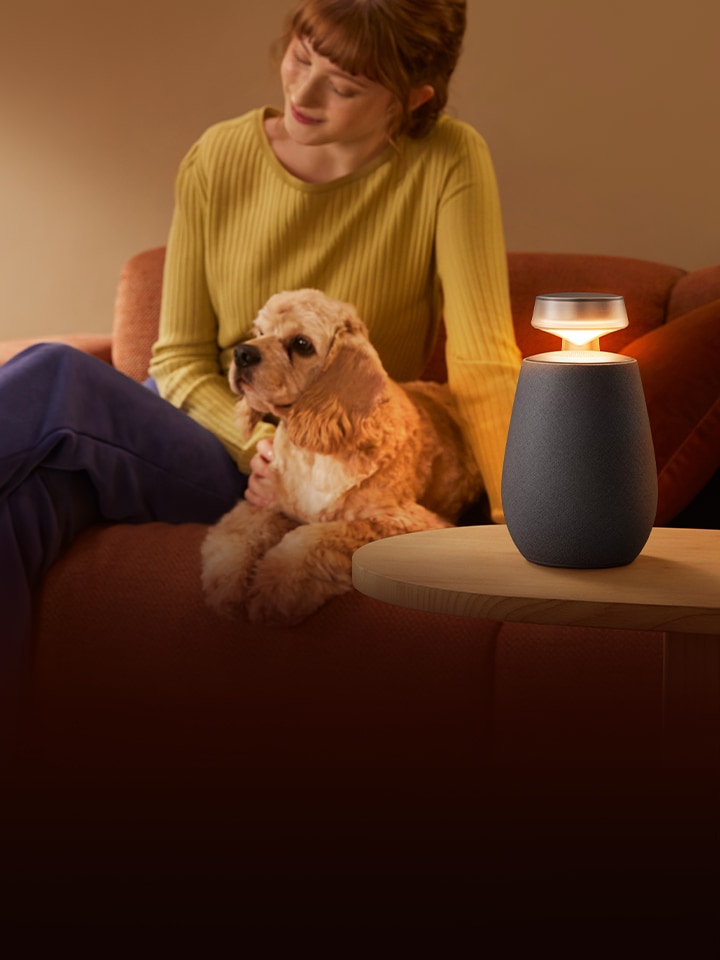 A woman replaxing with LG XBOOM XO2T with her dog on the sofa.