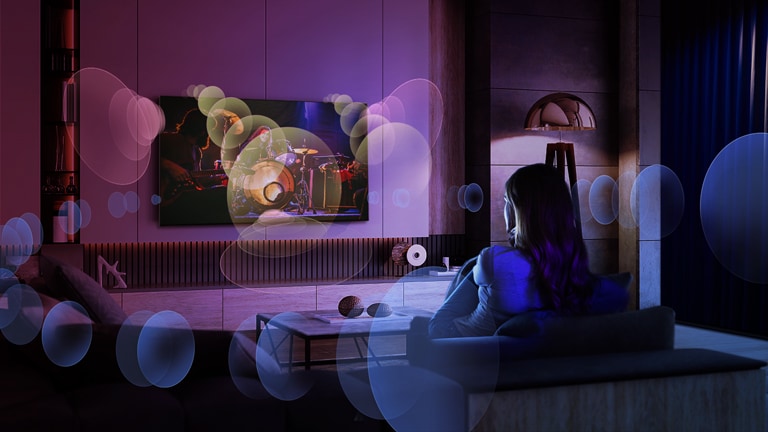 A woman sits on a couch watching a concert with bubbles depicting surround sound around her.