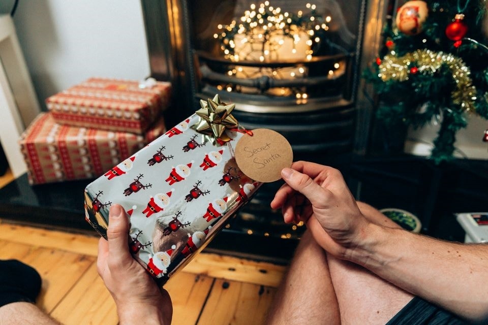 Die Hände einer Person präsentieren ein festlich verpacktes Weihnachts-Geschenk und zeigen ein von hochwertiges Luxus-Gadget für Männer.