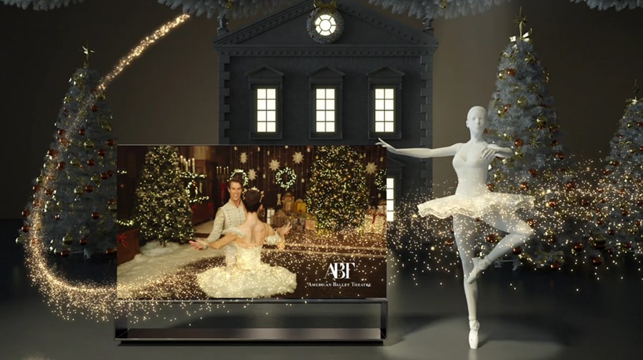 Aufrollbarer OLED TV R von LG SIGNATURE neben Weihnachtsbäumen und einer Ballerinastatue zeigt die Weihnachtsaufführung des Nussknackers des ABT auf dem Bildschirm.