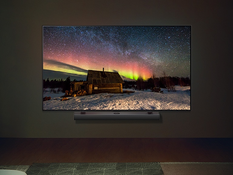 Téléviseur LG et barre de son LG dans un espace habitable moderne dans la nuit. L'image de l'aurore boréale est affichée avec les niveaux de luminosité idéaux.