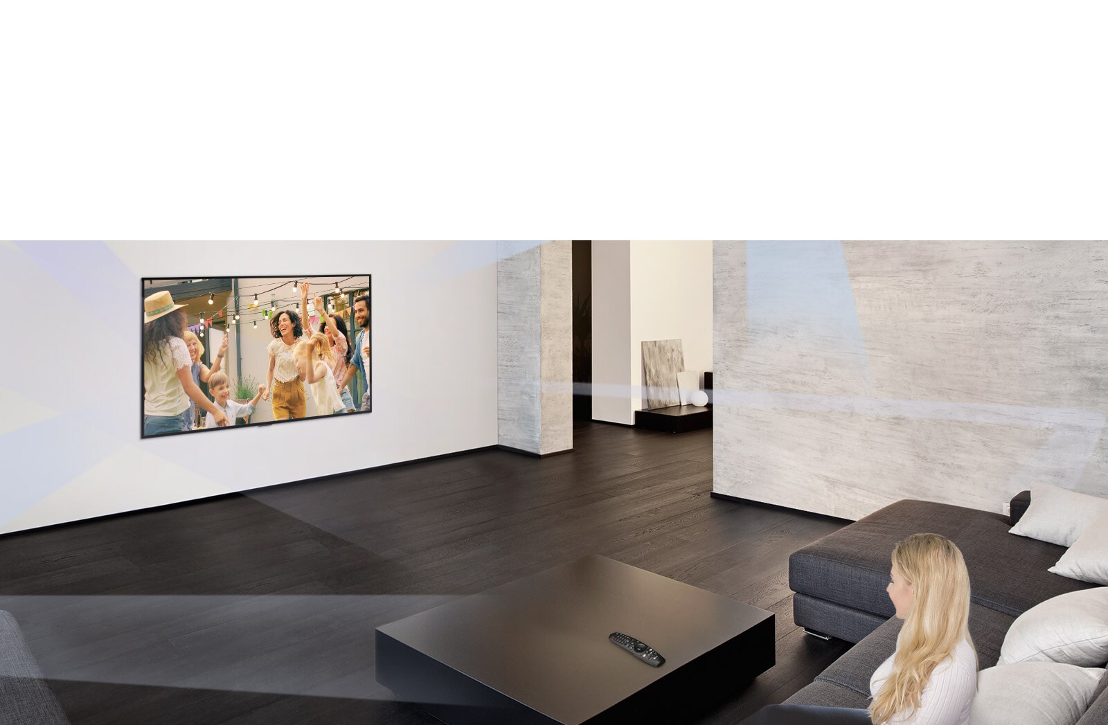 Une femme regarde des gens danser sur le téléviseur d’un grand salon au décor minimaliste.