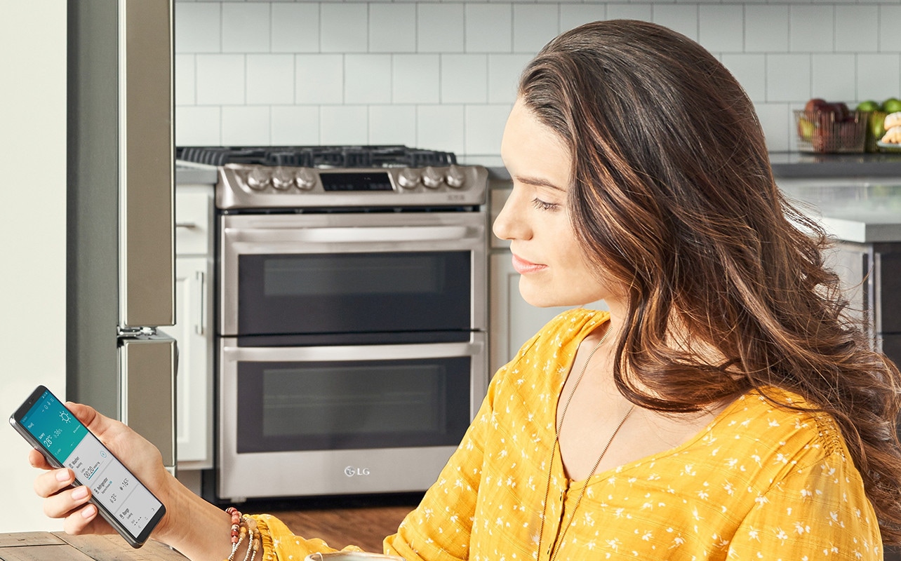 Une femme regarde son smartphone qui montre l’application LG ThinQ sur l’écran du smartphone.