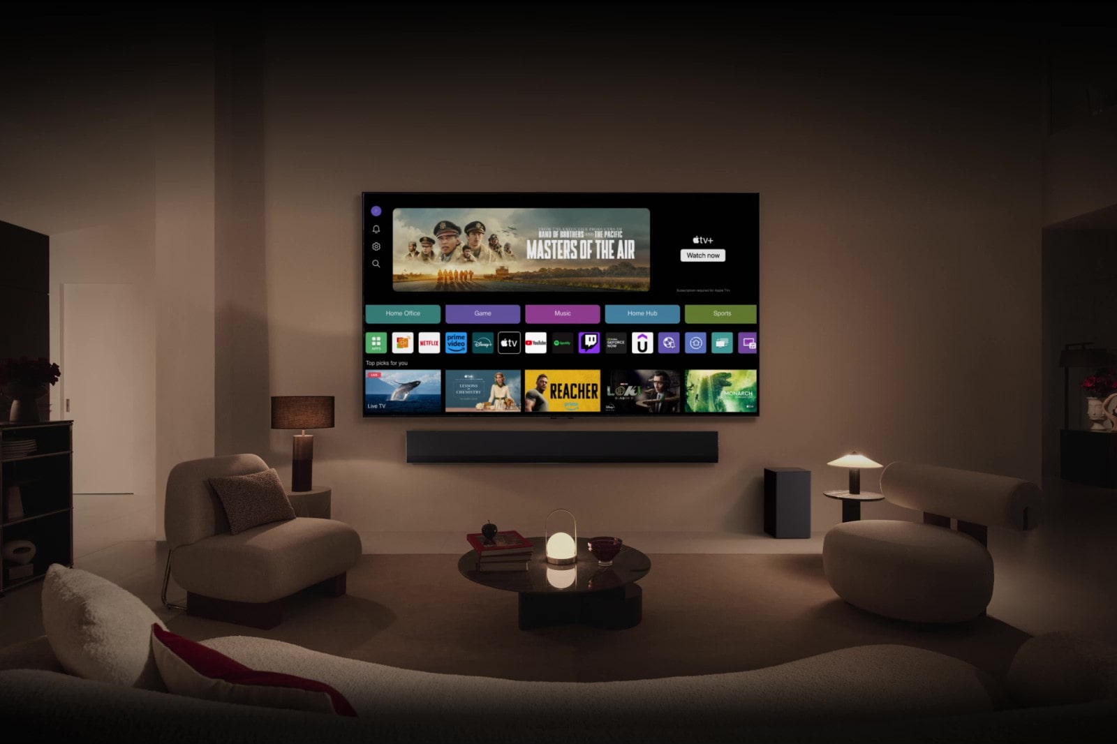 A close-up of an LG TV screen showing the buttons Home Office, Game, and Music over a banner for Masters of the Air zooms out to show the TV mounted on a wall in a living room. The following logos are displayed on the TV screen in the image: LG Channels, Netflix, Prime Video, Disney TV, Apple TV, YouTube, Spotify, Twitch, GeForce Now and Udemy.