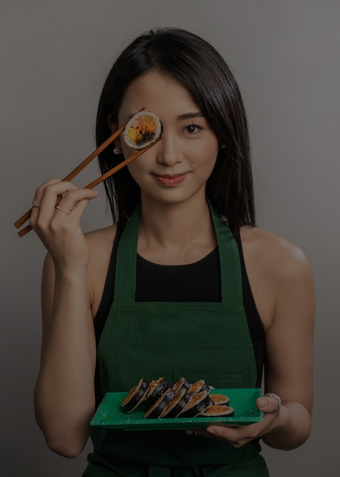 Tina Choi sosteniendo juguetonamente un trozo de kimbap cerca del ojo.