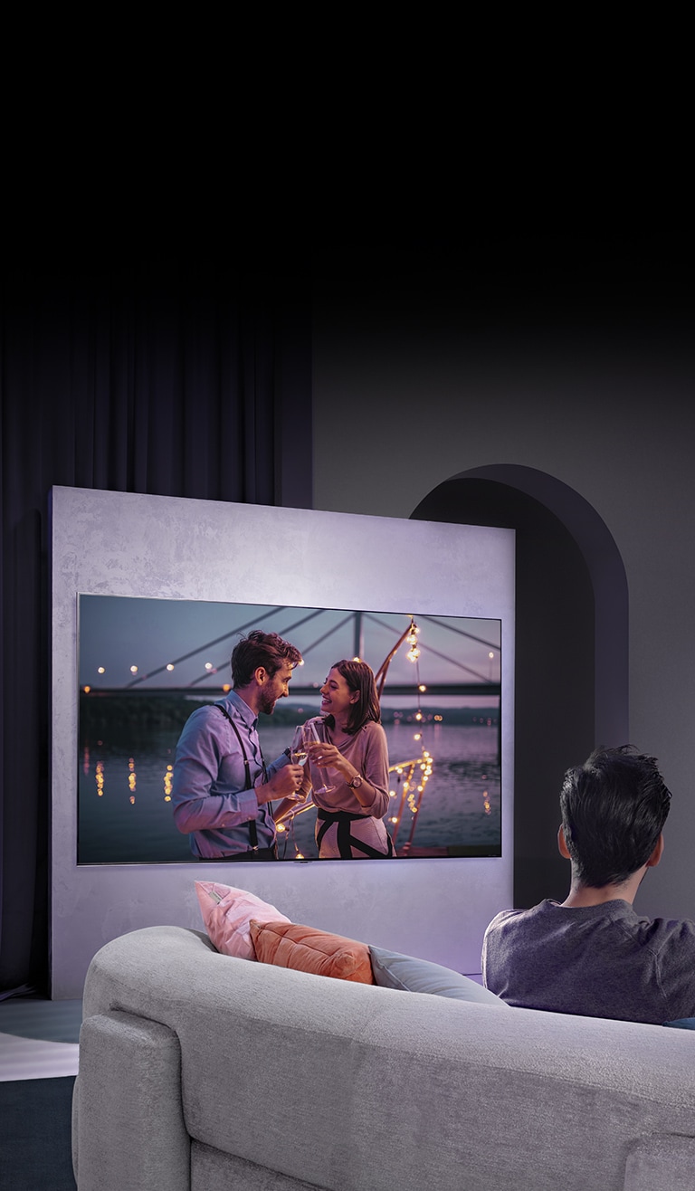 Diivanil istuv inimene naudib filmi seinal olevast suurest televiisorist.