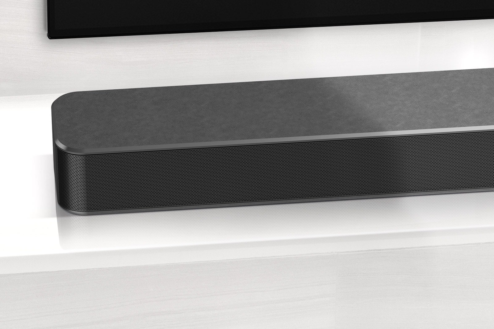 Close-up of LG Soundbar left corner. Bottom left side of TV is also visible. 