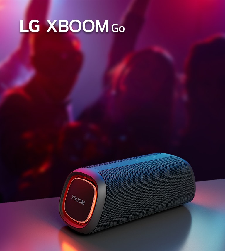 LG XBOOM Go XG7 on paigutatud metallist lauale ja põleb oranž valgustus. Laua taga naudivad inimesed muusikat.