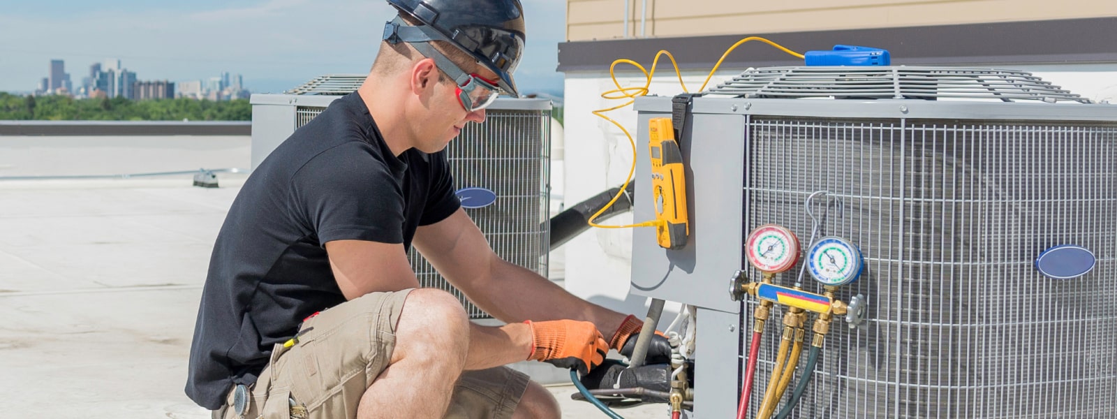 A man wearing a safety helmet is trying to replace a compressor outside.