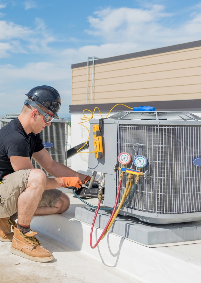 A man wearing a safety helmet is trying to replace a compressor outside.