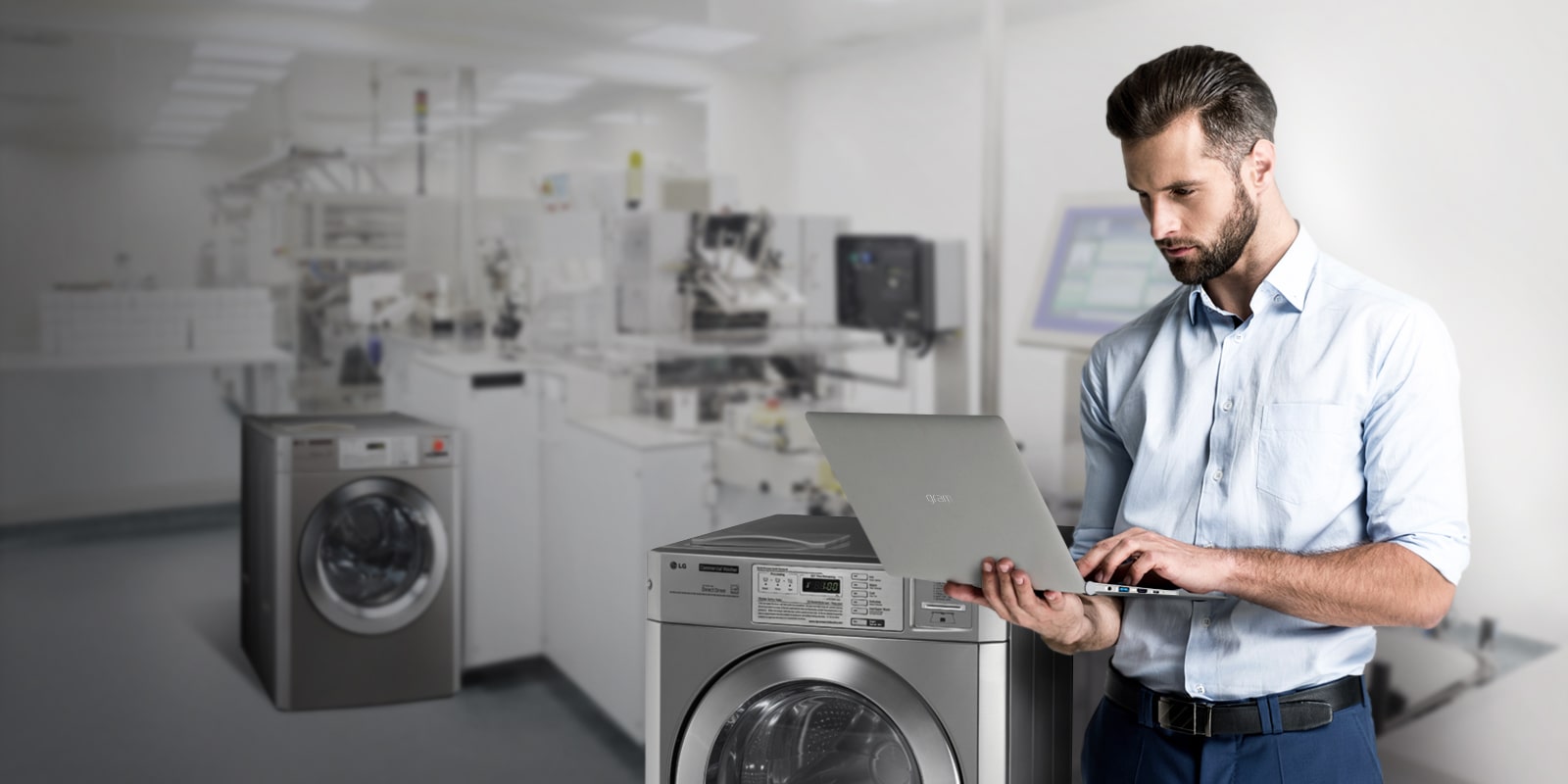 A professional man in business attire is using a laptop in a commercial laundry room equipped with the LG Commercial Laundry.