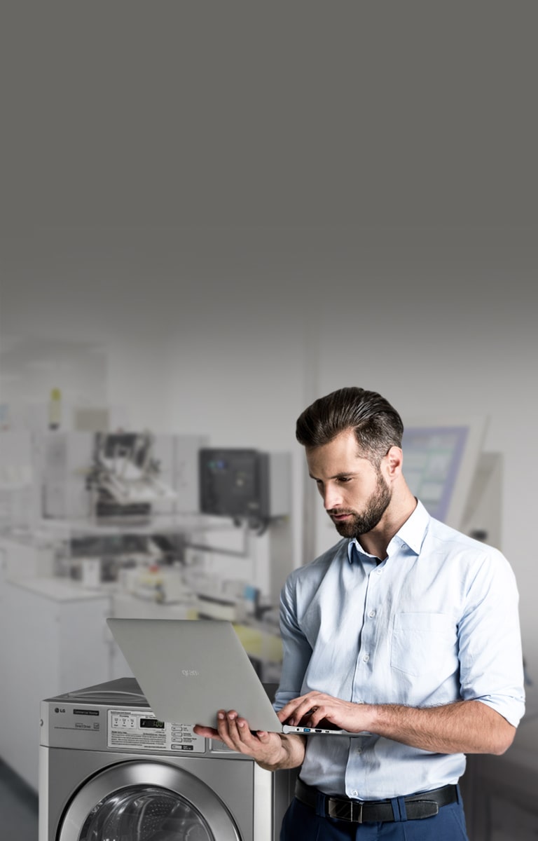 A professional man in business attire is using a laptop in a commercial laundry room equipped with the LG Commercial Laundry.