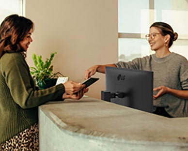 Friendly receptionist showing a woman where to sign on a digital tablet.	