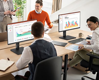 Employees sitting at office desks and having a conversation.	