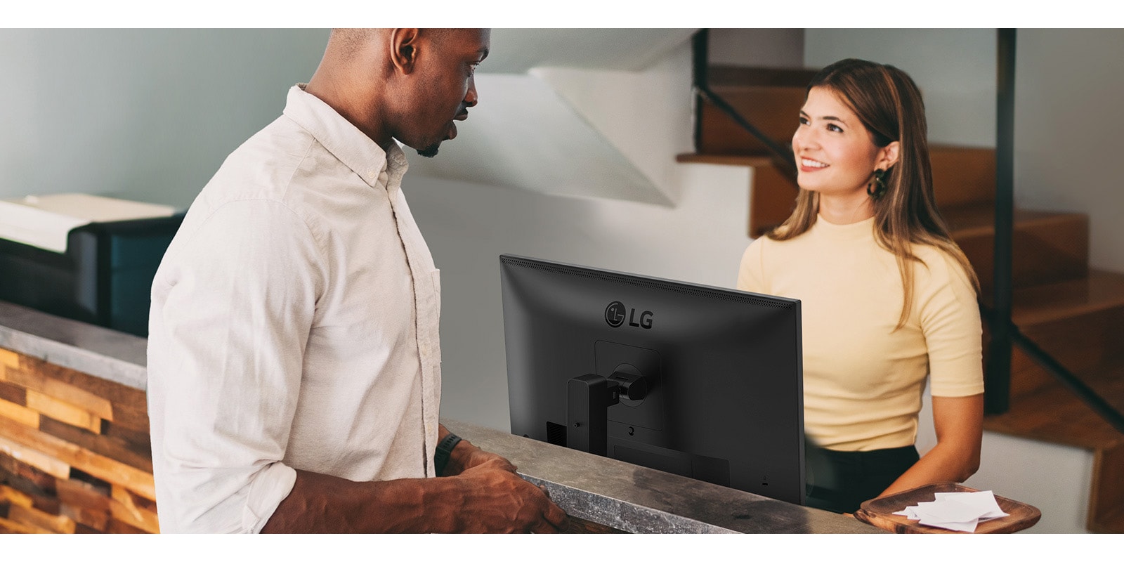 A female receptionist is talking to a man at the front desk.	