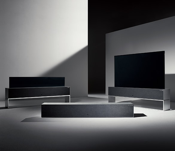 Three LG SIGNATURE OLED R TVs arranged in a dimmly lit space. Each TV is in a different mode, the central one in Zero View, one to the left in Line View, and one to the right in Full View.