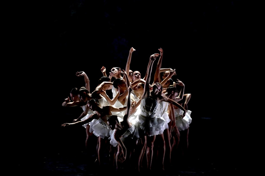 A group of female dancers in white tutus pose to form a flowery shape together.