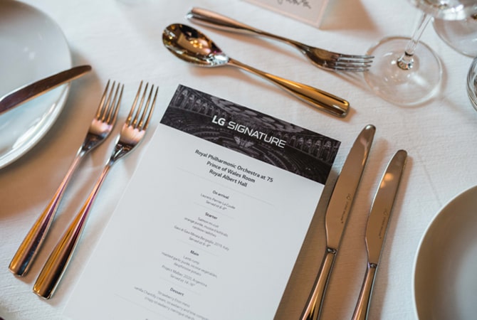 A menu with 'LG SIGNATURE' written at the top sits on a white table cloth with a fine dining table setting.