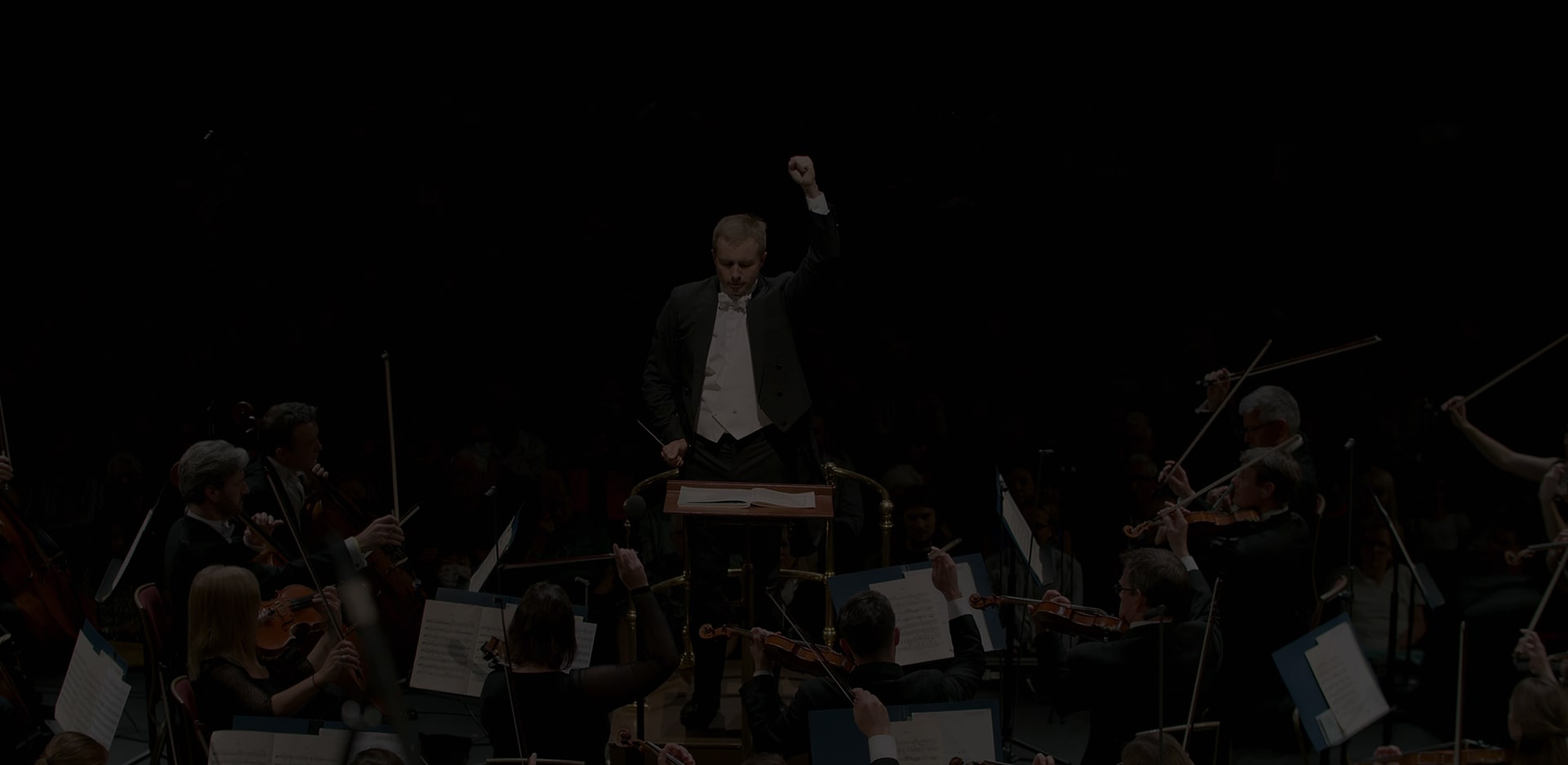 A conductor directs an orchestra. Overlayed text: 'The Musical Offering to the Whole World. #music #partnership'