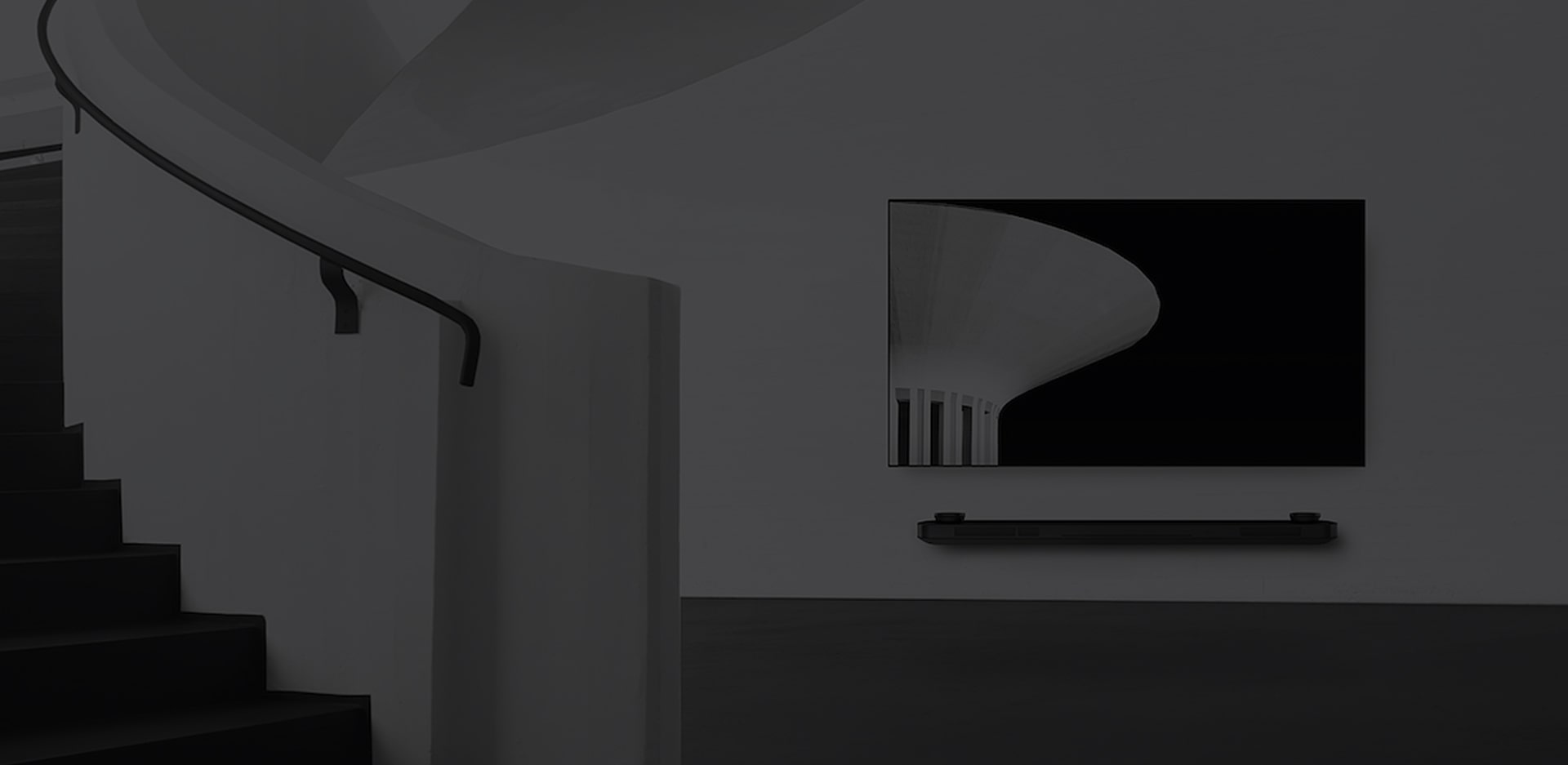 a black and white image of lg signature oled tv which is hung on the wall and to the left there is a spiral staircase