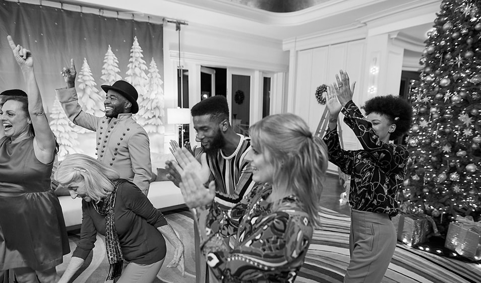 Six people clapping and laughing in a room decorated for Christmas