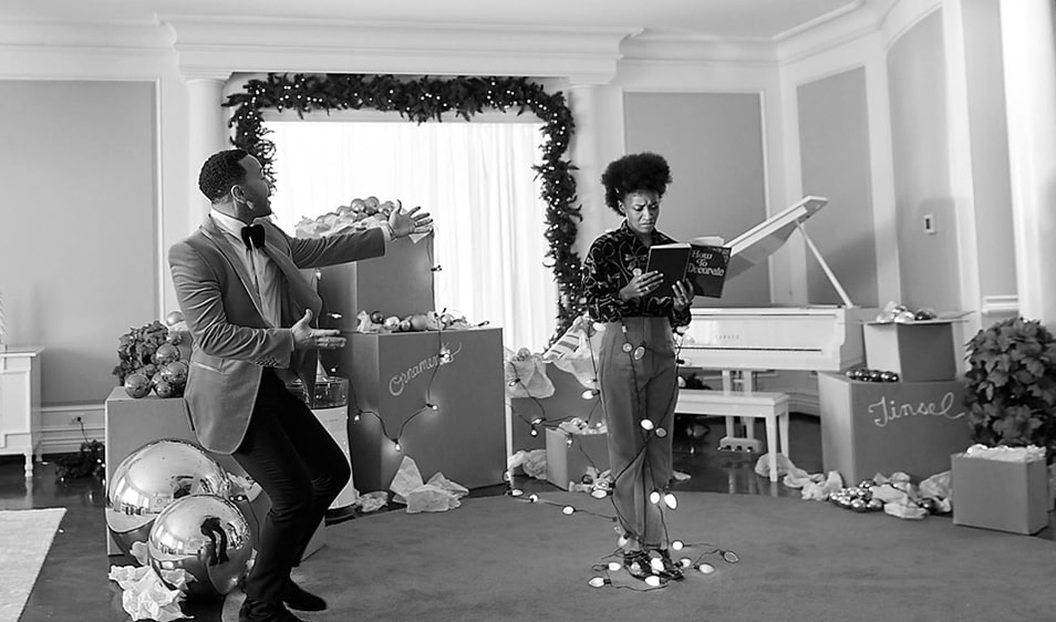 John Legend dancing next to a woman encircled in chrismas lights reading a book