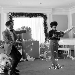 John Legend dancing next to a woman encircled in chrismas lights reading a book