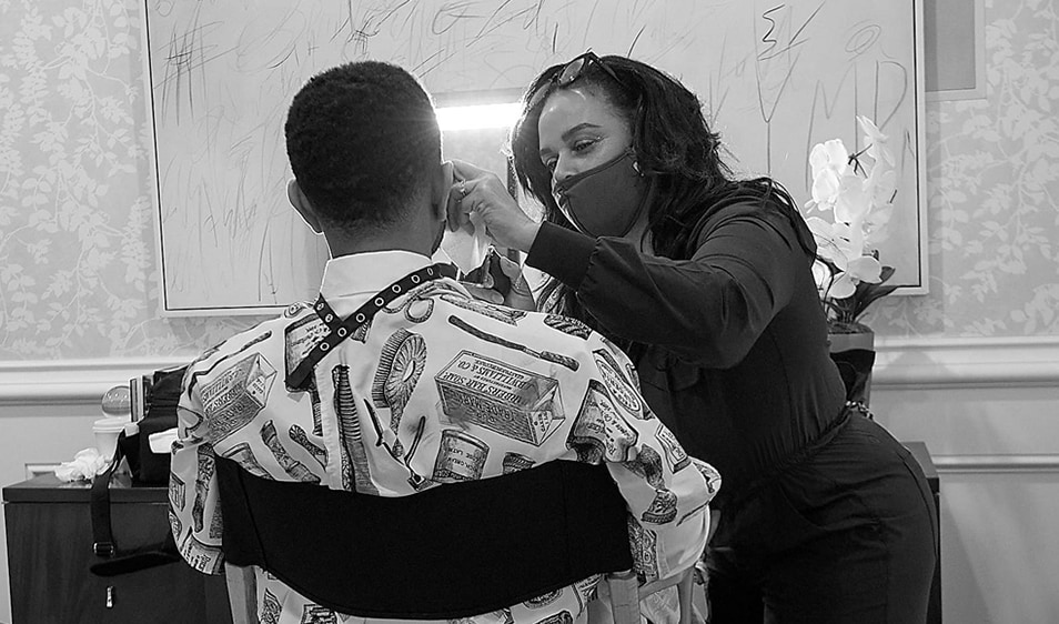 John Legend sitting in a makeup chair while a makeup artist works on him