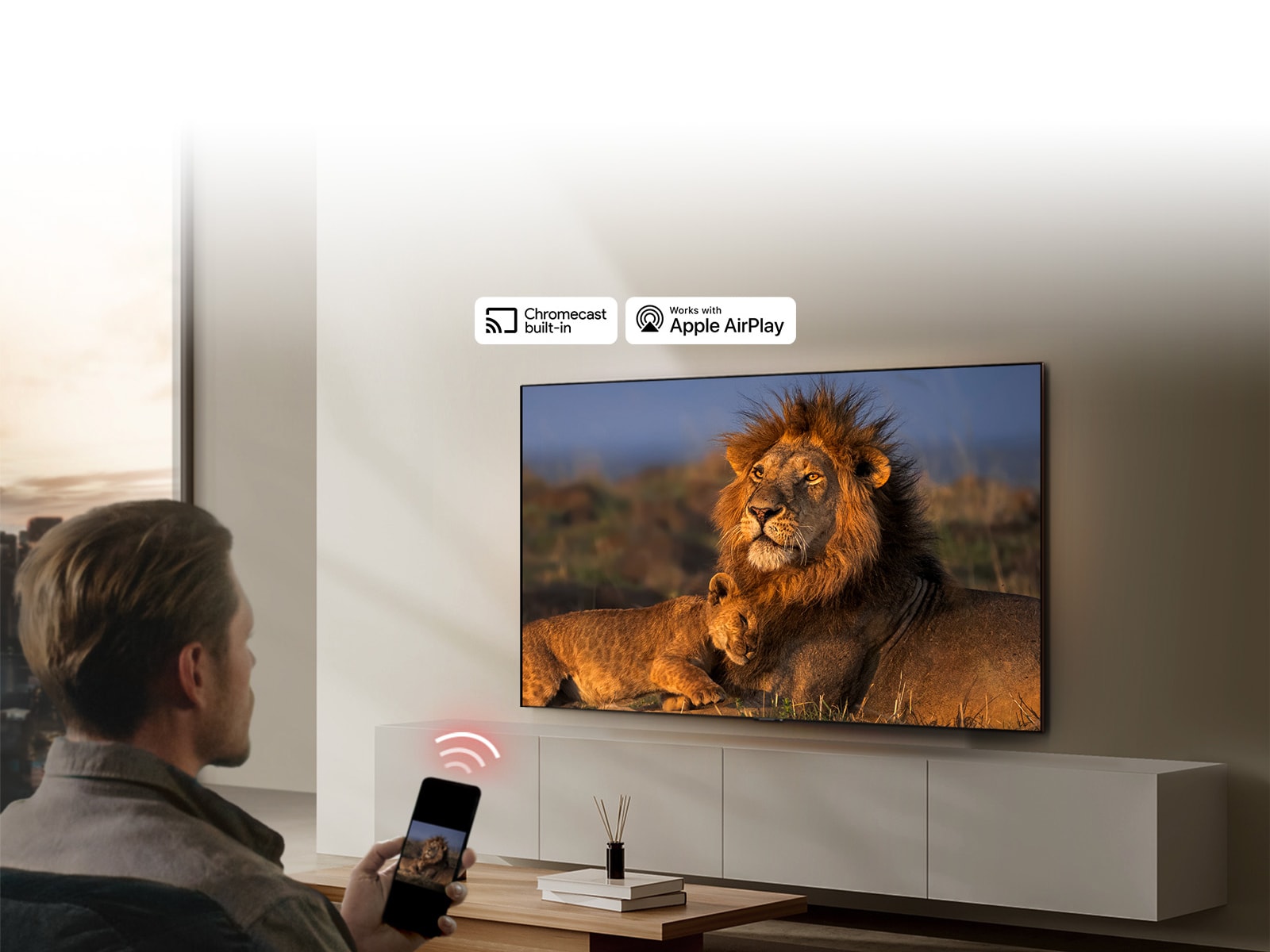 Televizor LG TV montiran na zidu dnevnog boravka, prikazuje se lav i mladunče lava. U prvom planu se prikazuje muškarac koji sjedi i drži mobitel u ruci na čijem se zaslonu vidi ista slika lavova. Grafički prikaz tri neonsko crvene zakrivljene trake prikazuje se točno iznad pametnog telefona usmjerenog prema televizoru.