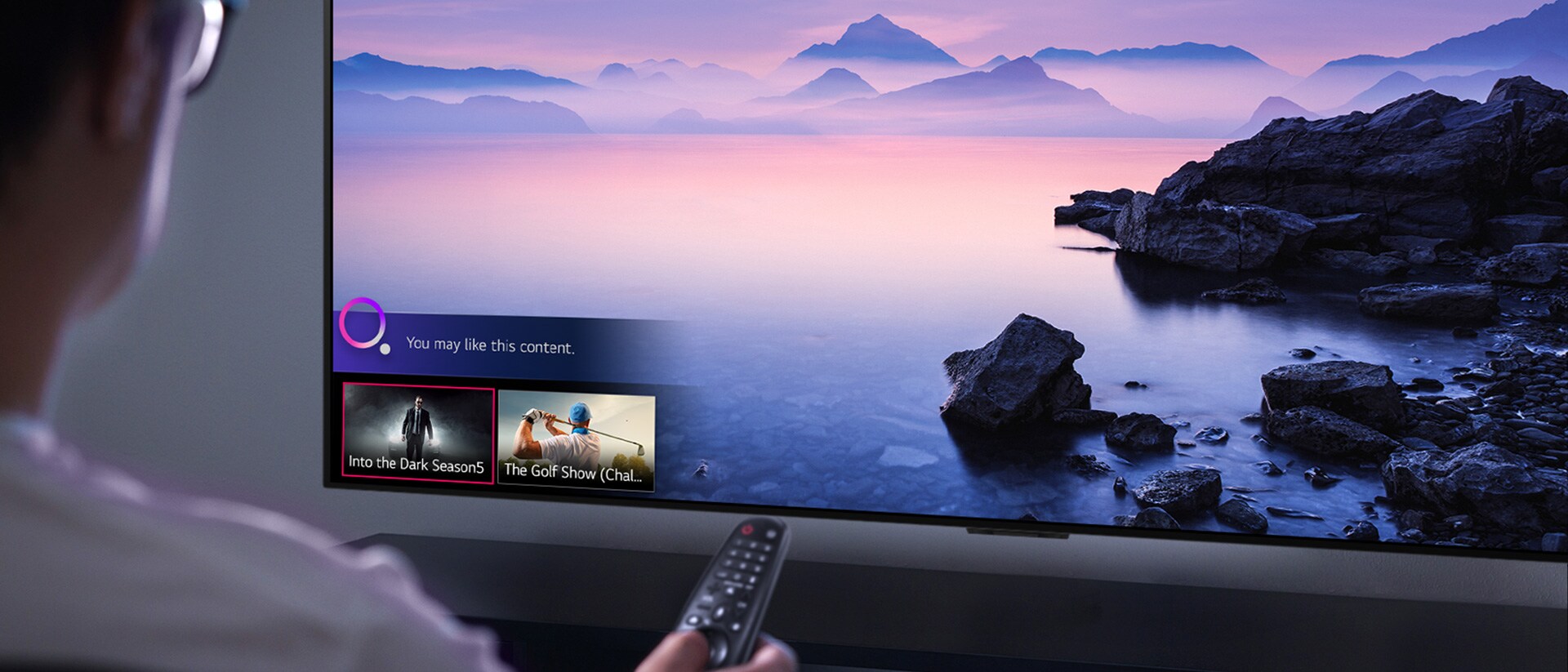 Prikaz izbliza muškarca koji bira što želi gledati na televizoru pomoću daljinskog upravljača, uz televizor na kojem je prikazan krajolik
