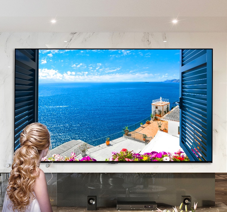 A képen egy nő látható hátulról, amint egy ablakon keresztül nézi a kék tengert és fehér épületeket. Az oldalt lefelé görgetve a kép egyre nagyobb nagyításban látható, egyre több részletet mutatva meg a szobából, végül felfedve, hogy az ablak valójában egy LG QNED MiniLED TV.