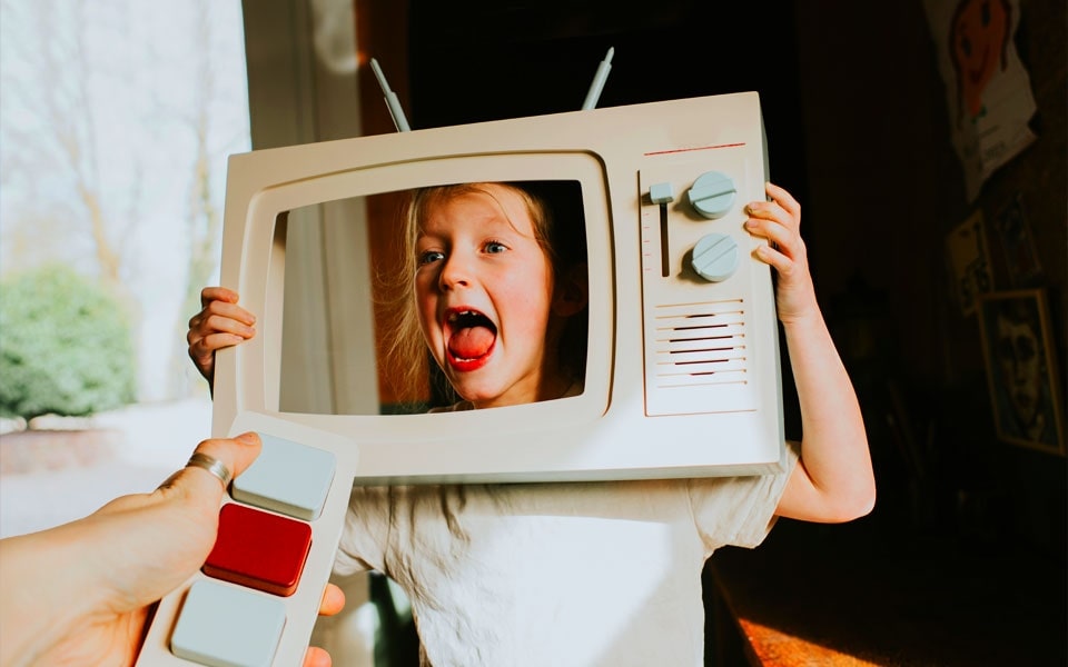 Gyermek, aki egy TV-t tart a kezében, a felnőtt kezében egy játék tv távirányítóval, amely a TV kalibrálásának folyamatát ábrázolja.