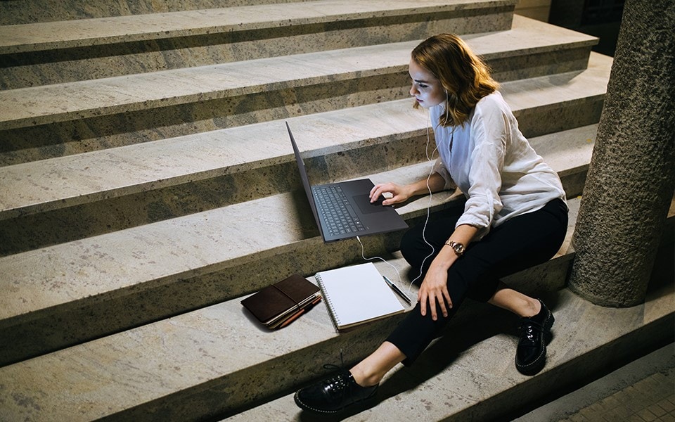 Egy nő ül a lépcsőn kívül dolgozik rajta laptop