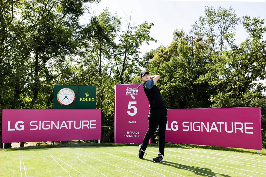Una golfista vestita di nero effettua un colpo in una tee box con il numero 5, con cartelli che pubblicizzano LG SIGNATURE sullo sfondo.