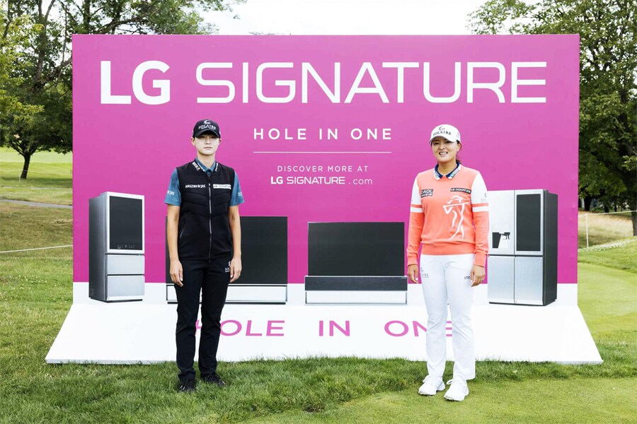 Un annuncio LG Signature rosa su un campo da golf, con immagini dei prodotti e due persone in primo piano su un paesaggio verdeggiante.
