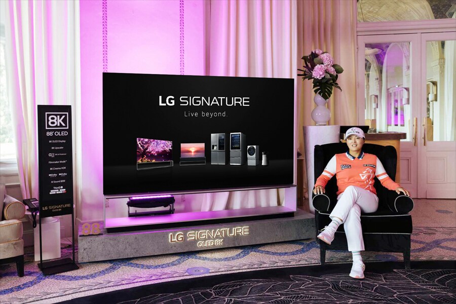 Un soggiorno moderno con un grande TV LG SIGNATURE e una persona seduta in una poltrona nera circondata da un arredamento contemporaneo.