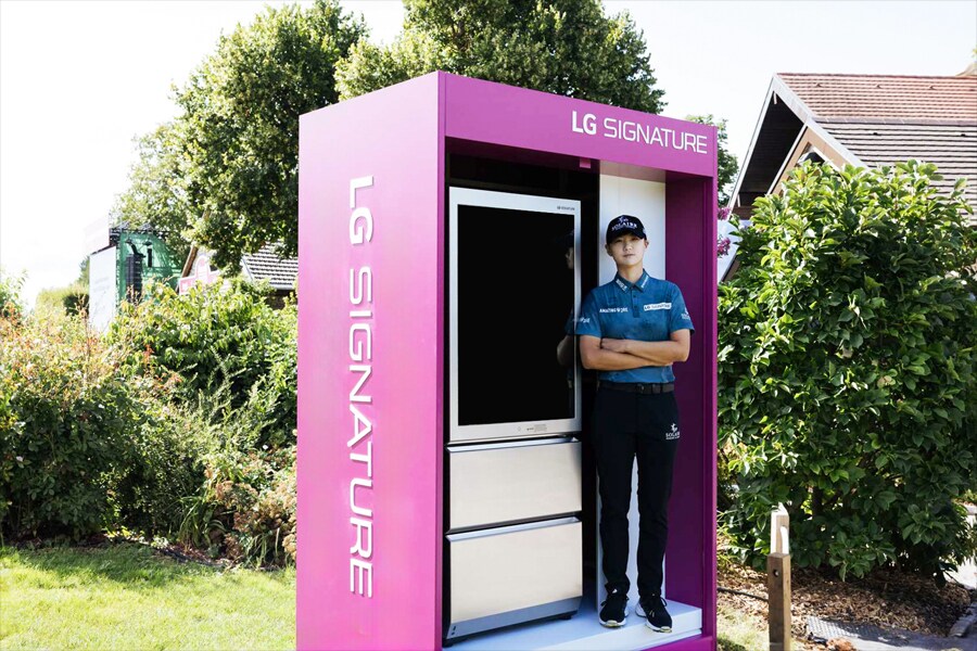 Uno stand LG SIGNATURE viola con uno schermo nero, accompagnato da una donna al suo fianco.