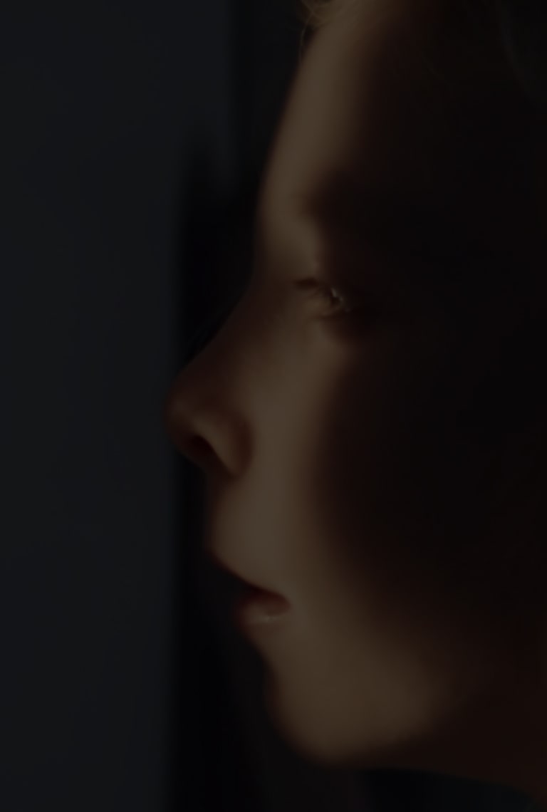 Inquadratura in primo piano del volto di una ragazza, parzialmente in ombra, parzialmente illuminato mentre sbircia fuori da un nascondiglio.