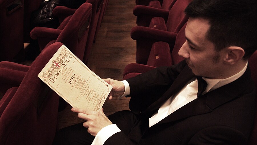 Un uomo seduto al Teatro alla Scala consulta un programma.