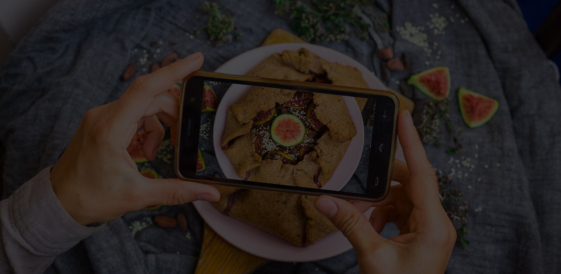 Un paio di mani tengono uno smartphone sopra un tortino di fichi mentre viene scattata una foto. La scritta 'Siamo ciò che mangiamo' è sovrapposta all'immagine.