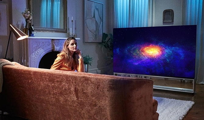 Olivia Palermo si rilassa sulla sua poltrona, guardando la televisione sul suo LG SIGNATURE OLED 8K TV.