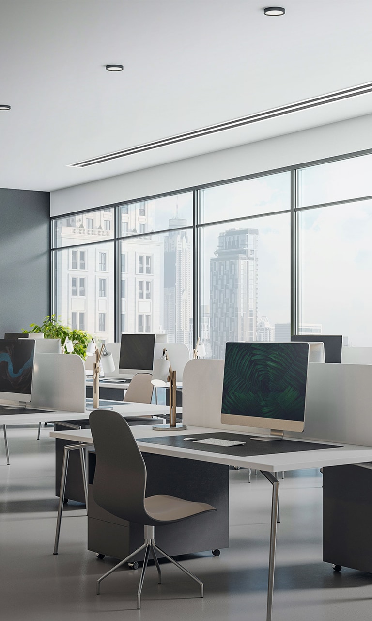 In an office with floor-to-ceiling windows showcasing the city skyline, desks, and computers, the LG Ceiling Concealed Duct maintains the office's clean and modern aesthetic.