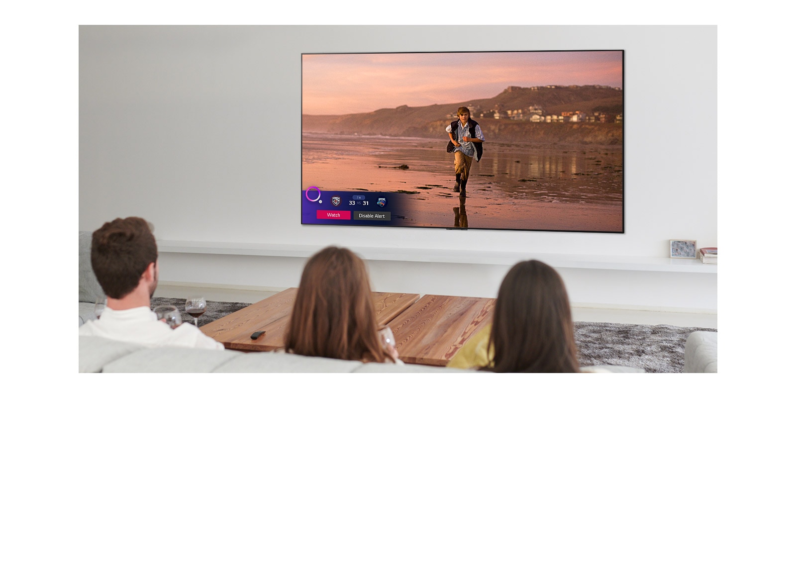 Three people watching TV screen showing a scene from a fantasy movie with a Sports Alert