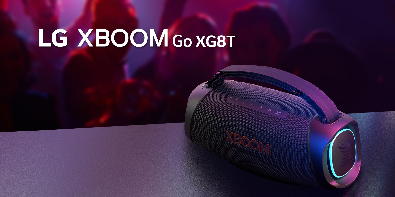 LG XBOOM Go XG8T padėtas ant metalinio stalo su įjungtu oranžiniu apšvietimu. Už stalo žmonės mėgaujasi muzika.